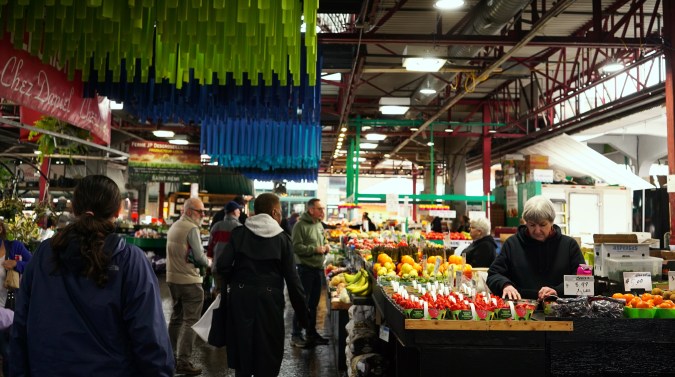 nterior del mercado Jean-Talon de Montreal con puestos de fruta y una instalación de tubos de colores en el techo