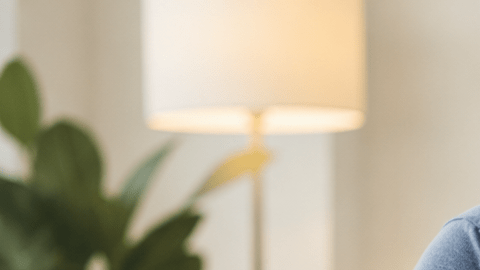 Una persona adulta sentada en su casa con una mano en el pecho, expresión de preocupación, teléfono cerca, ambiente realista y sobrio, sin dramatizar ni mostrar emergencia explícita.