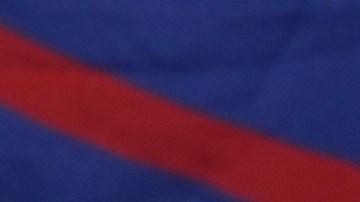 Un hombre pasa junto a una enorme bandera cubana mientras un grupo de cubanos se reúne para sostener pancartas y ondear banderas horas después de que los fiscales federales anunciaran cargos contra el expresidente cubano Raúl Castro.