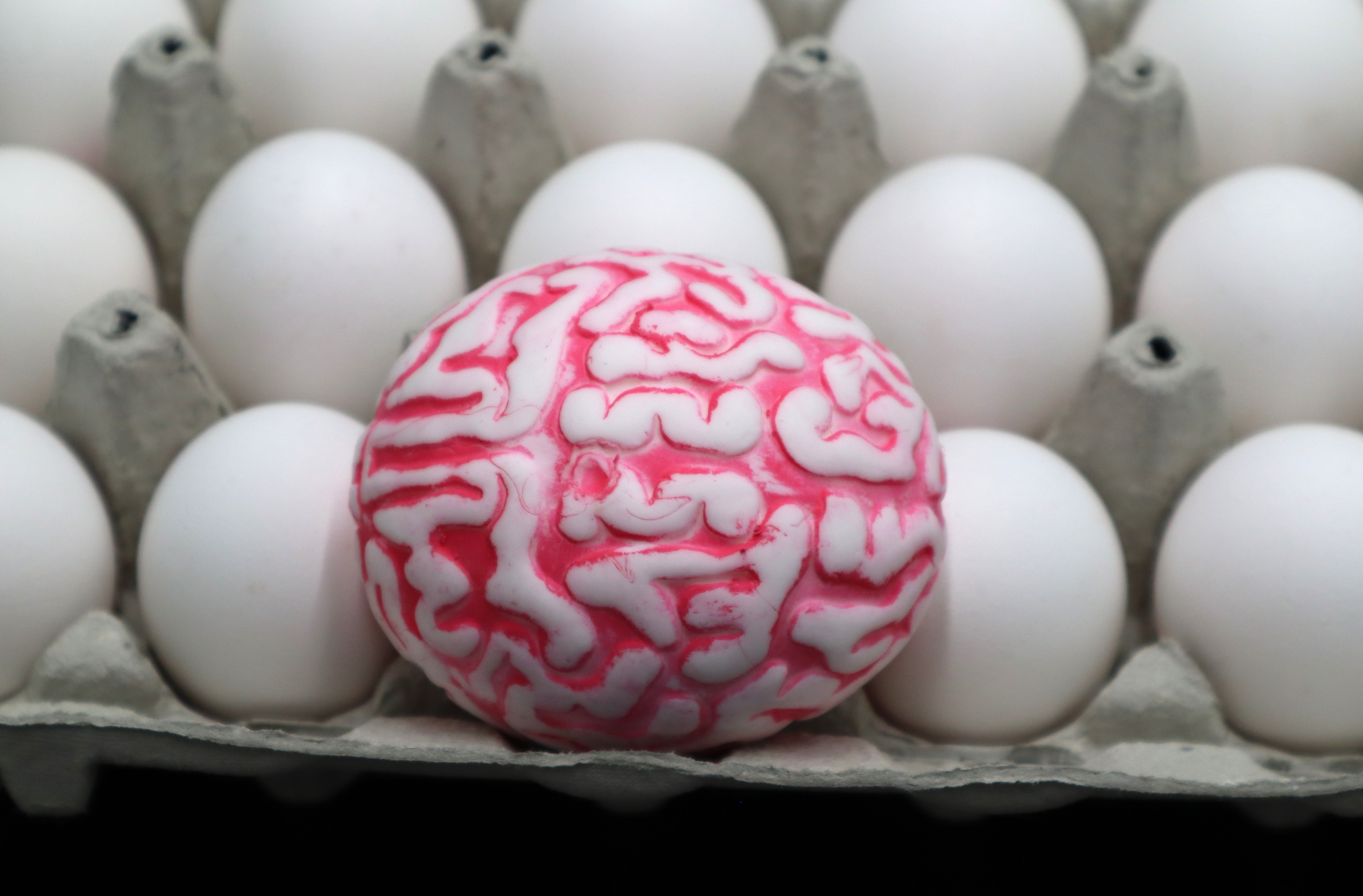 Un huevo tallado como un cerebro en medio de huevos blancos