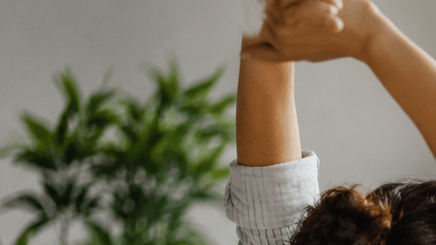 Mujer haciendo una pausa activa mientras trabaja sentada frente a una computadora en una oficina con luz natural.