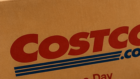 Pastel personalizado de Costco junto a bandejas de comida para fiestas y una caja de entrega a domicilio, en una cocina.