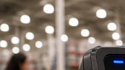 Persona usando un teléfono móvil para pagar de forma digital en una tienda Costco, junto a una terminal de cobro sin contacto.