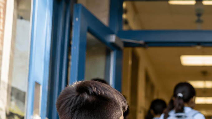 Trabajadora escolar acompaña a estudiantes en la entrada de una escuela pública de Nueva York, en una imagen alusiva a las nuevas vacantes de NYC Public Schools.